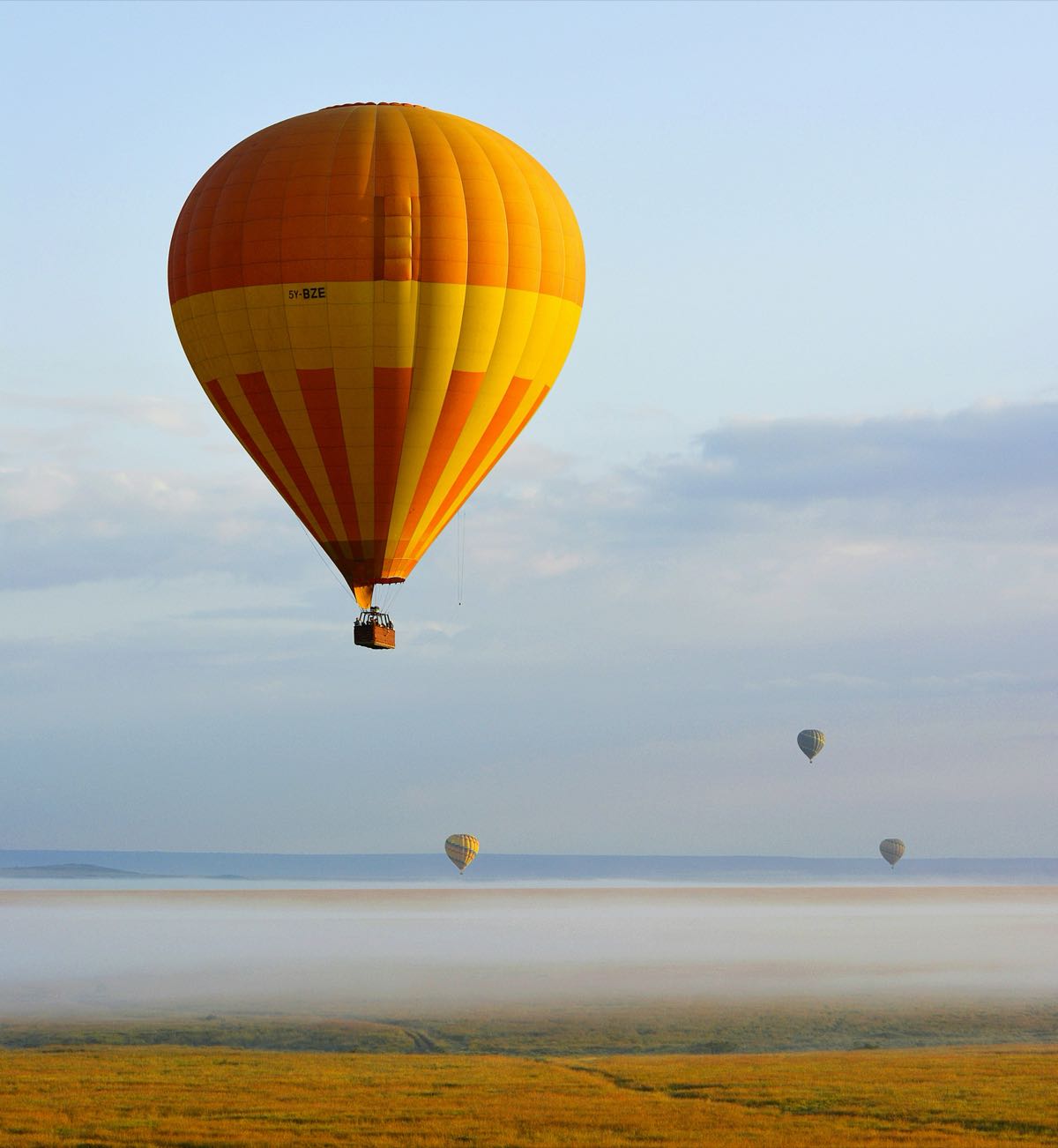 Hot air balloon in flight over the Masai Mara savanna at sunrise with mist below, Kenya