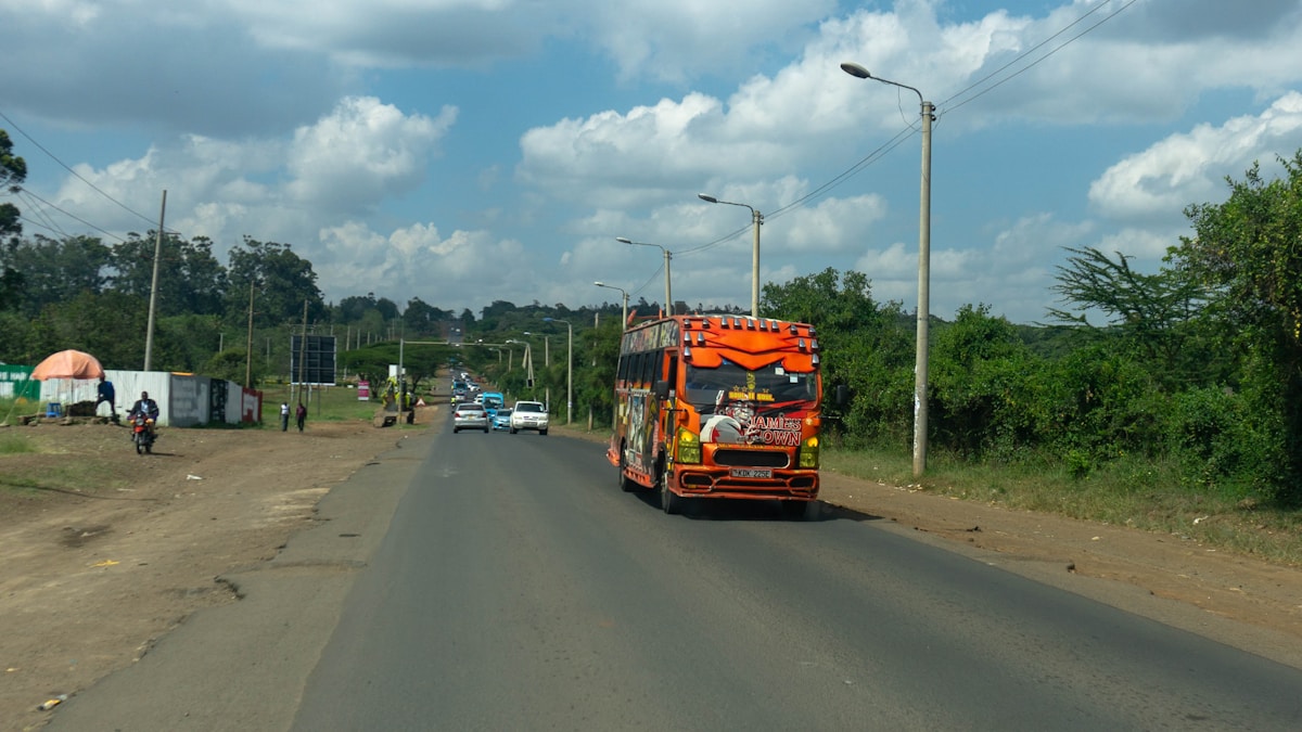 Colourful orange Kenyan matatu bus on a lush green-lined road, western Kenya