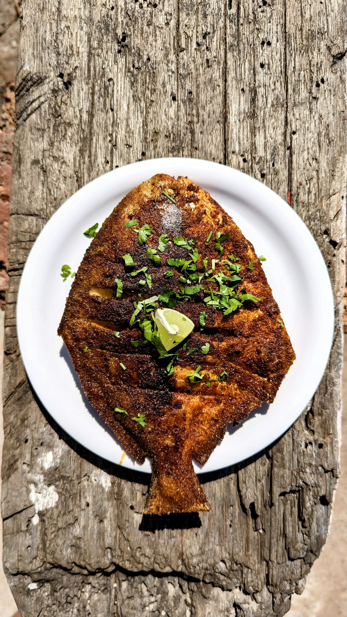 Whole spiced fried fish on a plate outdoors, representing Swahili coastal cuisine