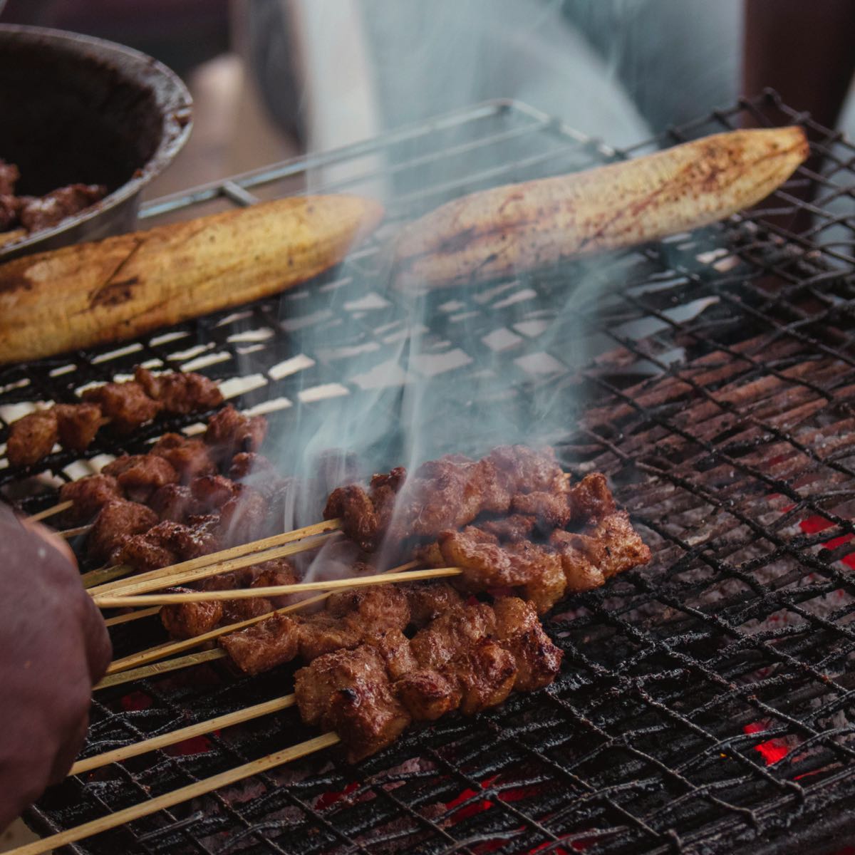 Meat skewers and a plantain grilling over hot charcoal at an open-air barbecue