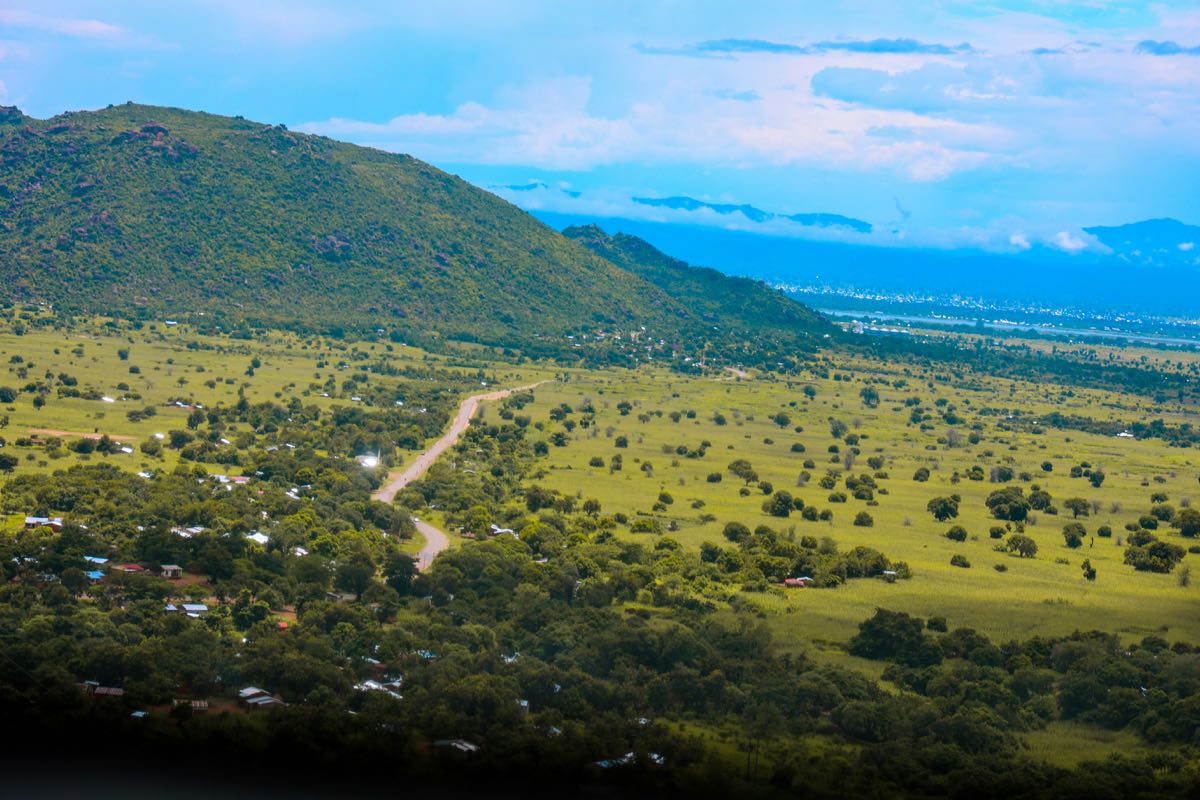 Aerial view of lush green rolling hills and valley with dirt road winding through Kenya's landscape during the long rains
