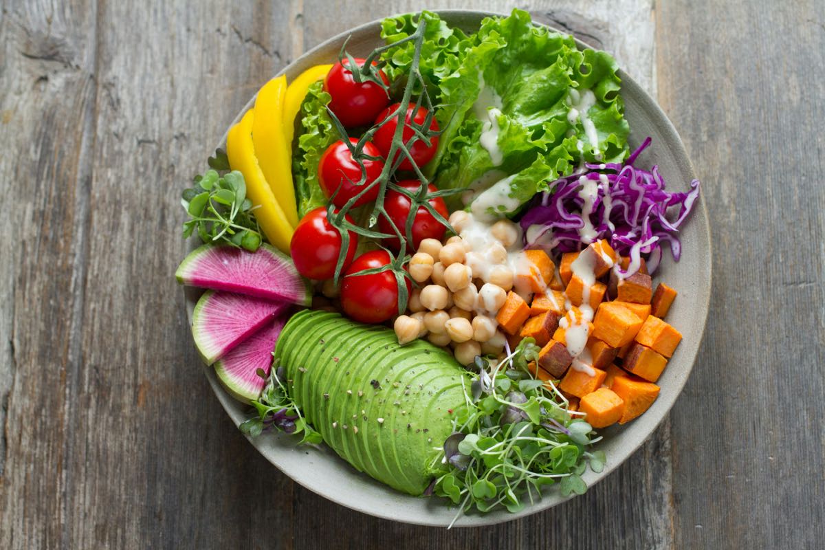 Colourful vegan bowl with avocado, cherry tomatoes, chickpeas, sweet potato, and mixed greens