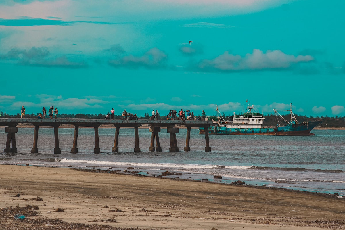 Fishing pier at Malindi with a cargo vessel anchored offshore and people walking on the jetty, Kenya coast